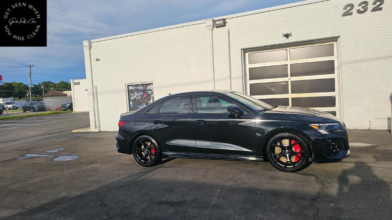 Black Audi sedan with red brake calipers parked outside a building with garage door, number 232.