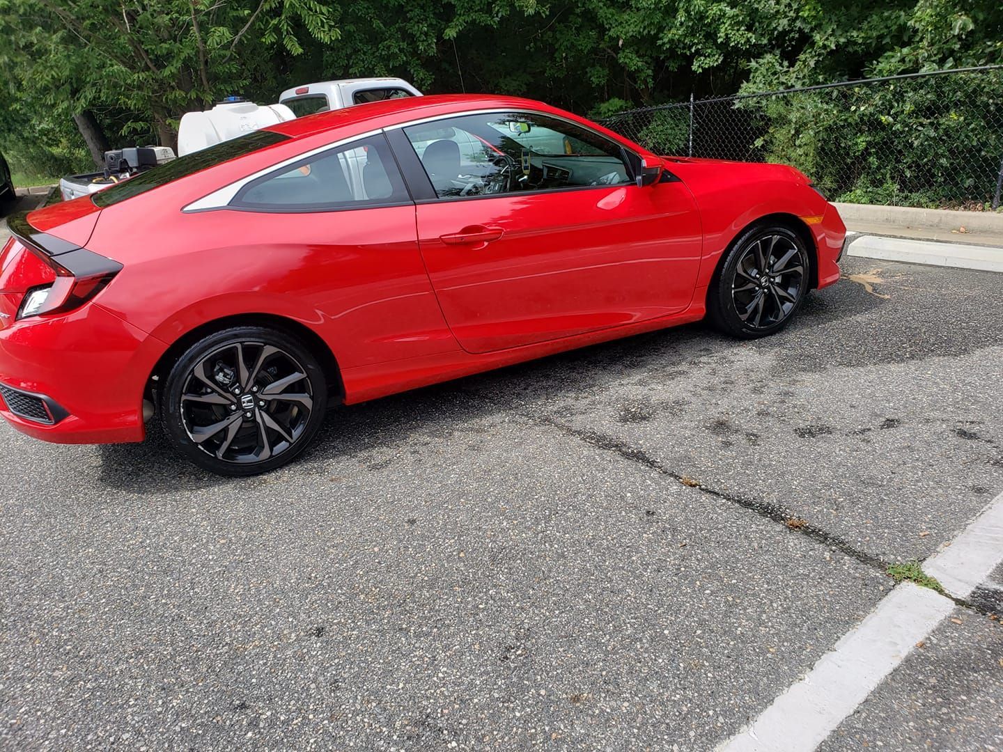 Red Honda Civic coupe parked on asphalt. Black wheels, sunlight.