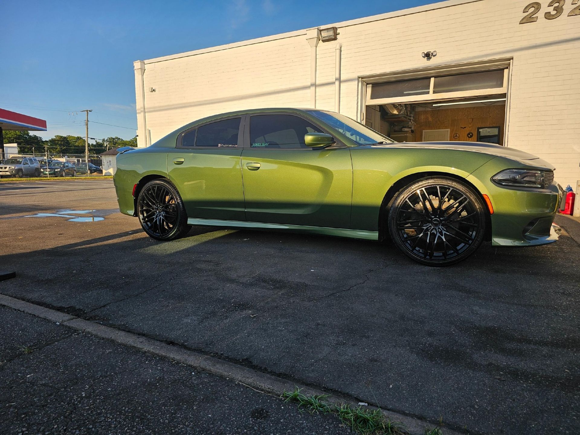 Green Dodge Charger parked in front of a white building with black wheels and tinted windows.