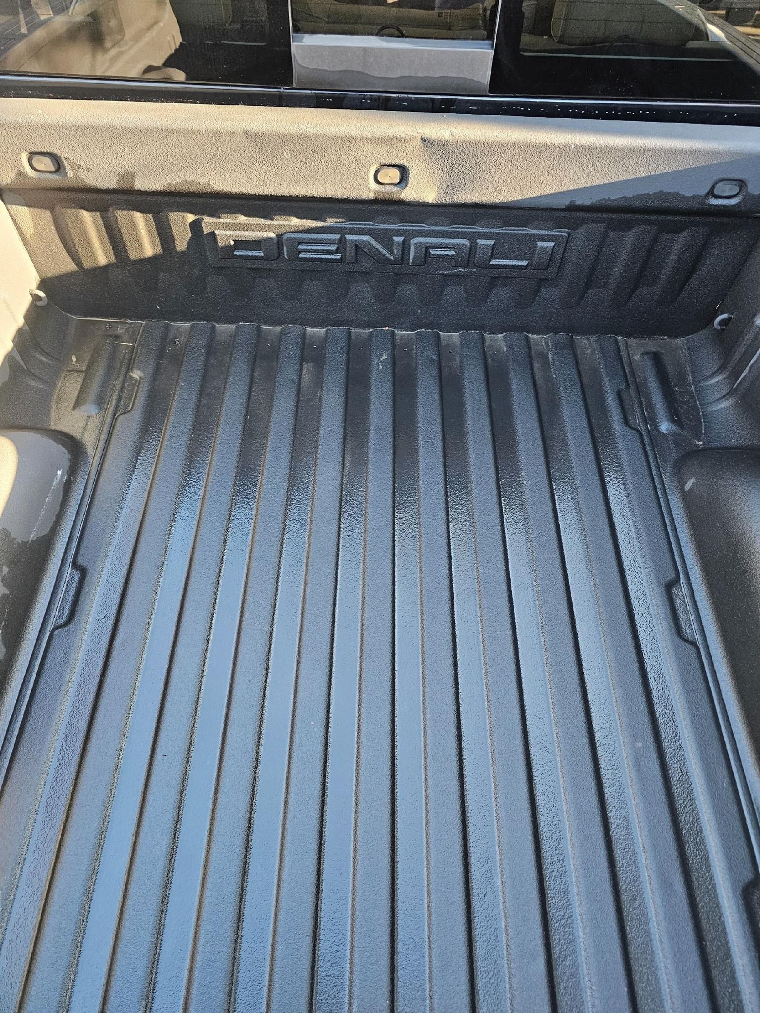 Black truck bed with DENALI logo, textured floor, vertical grooves, and tie-down points.