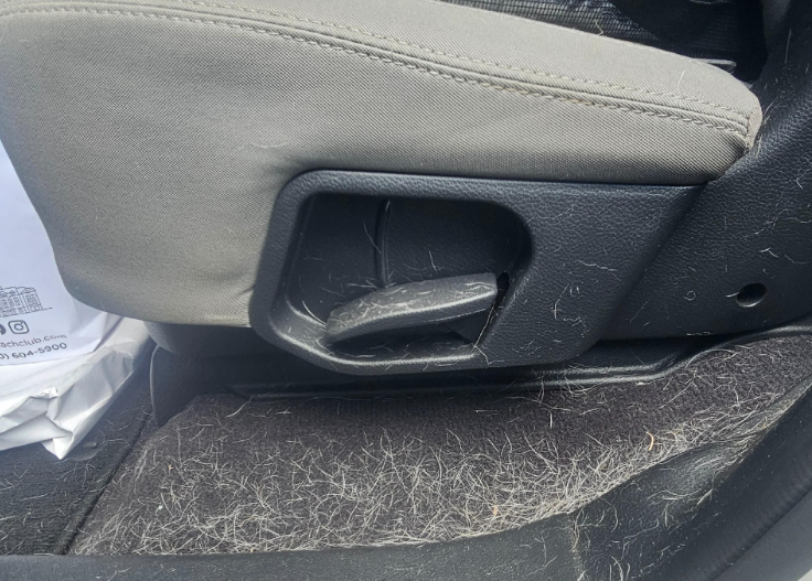Car seat and floor covered in light-colored animal fur. Beige seat with black adjustment lever.