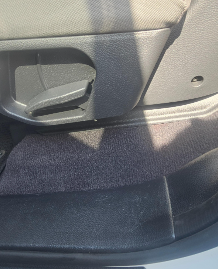 Car interior: black seat side with lever, gray carpet, and dark trim.