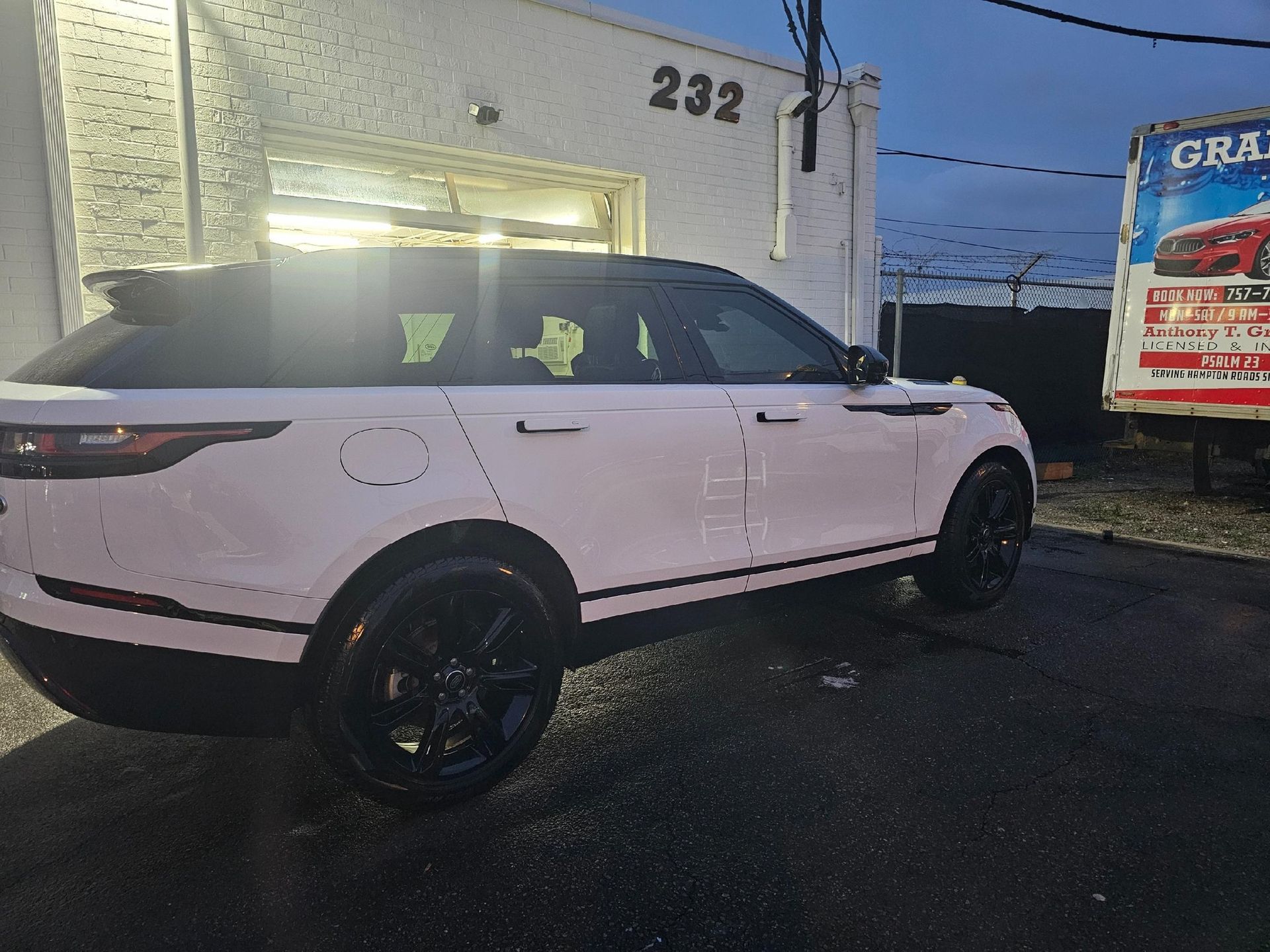 White Range Rover parked outside a building with the number 232. Black wheels.
