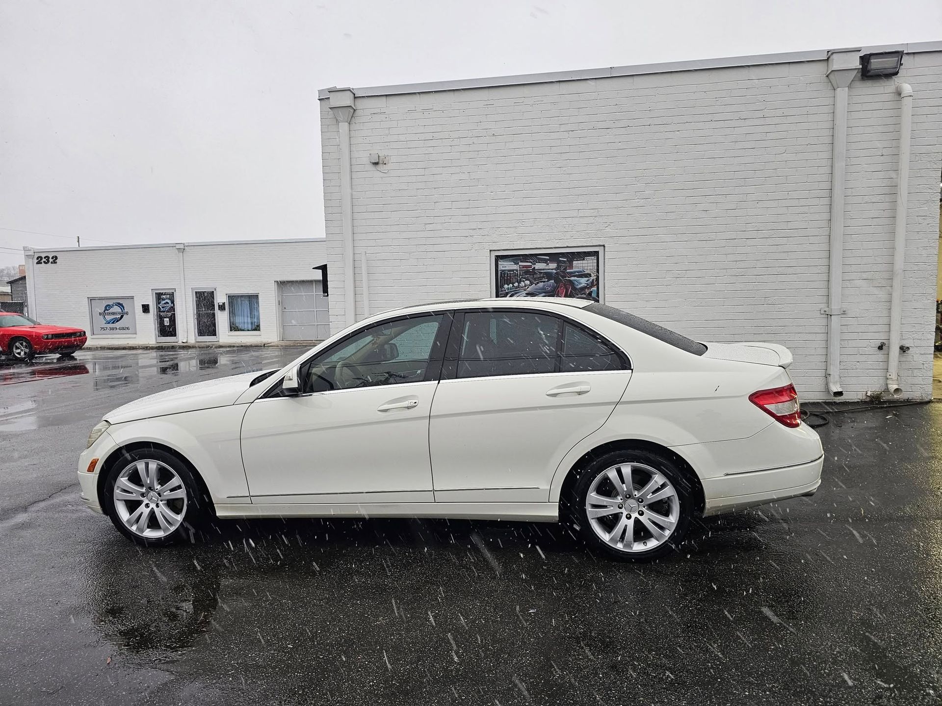 White Mercedes-Benz sedan parked on a wet street next to a white building; snowy weather.
