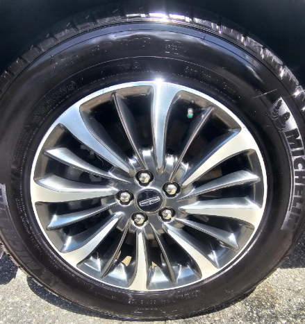 Black tire with a silver and black rim on a vehicle, showing a Lincoln logo.