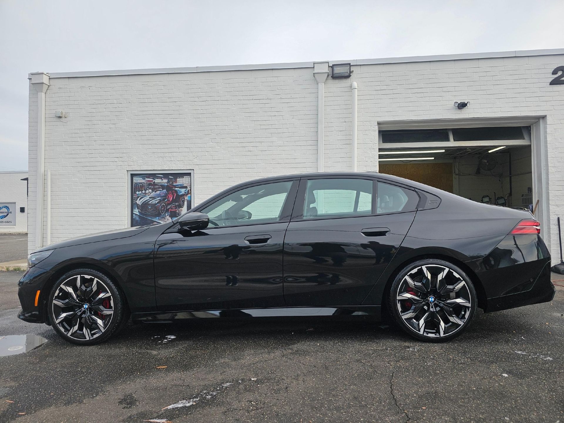 Black sedan with custom black and chrome rims parked in front of a white building with garage door.