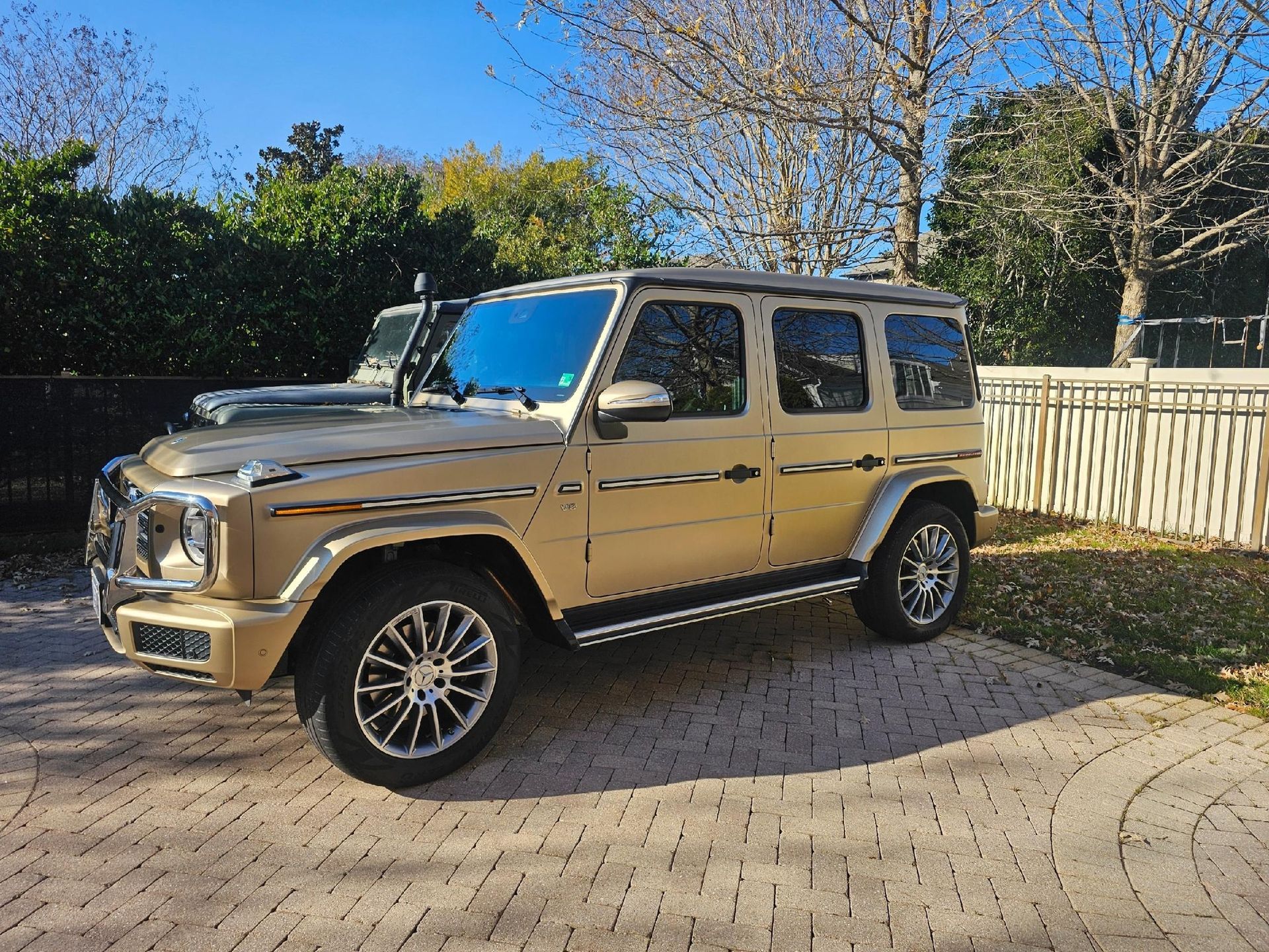 Gold SUV parked on a brick driveway, with a second SUV visible behind it. Sunny day.