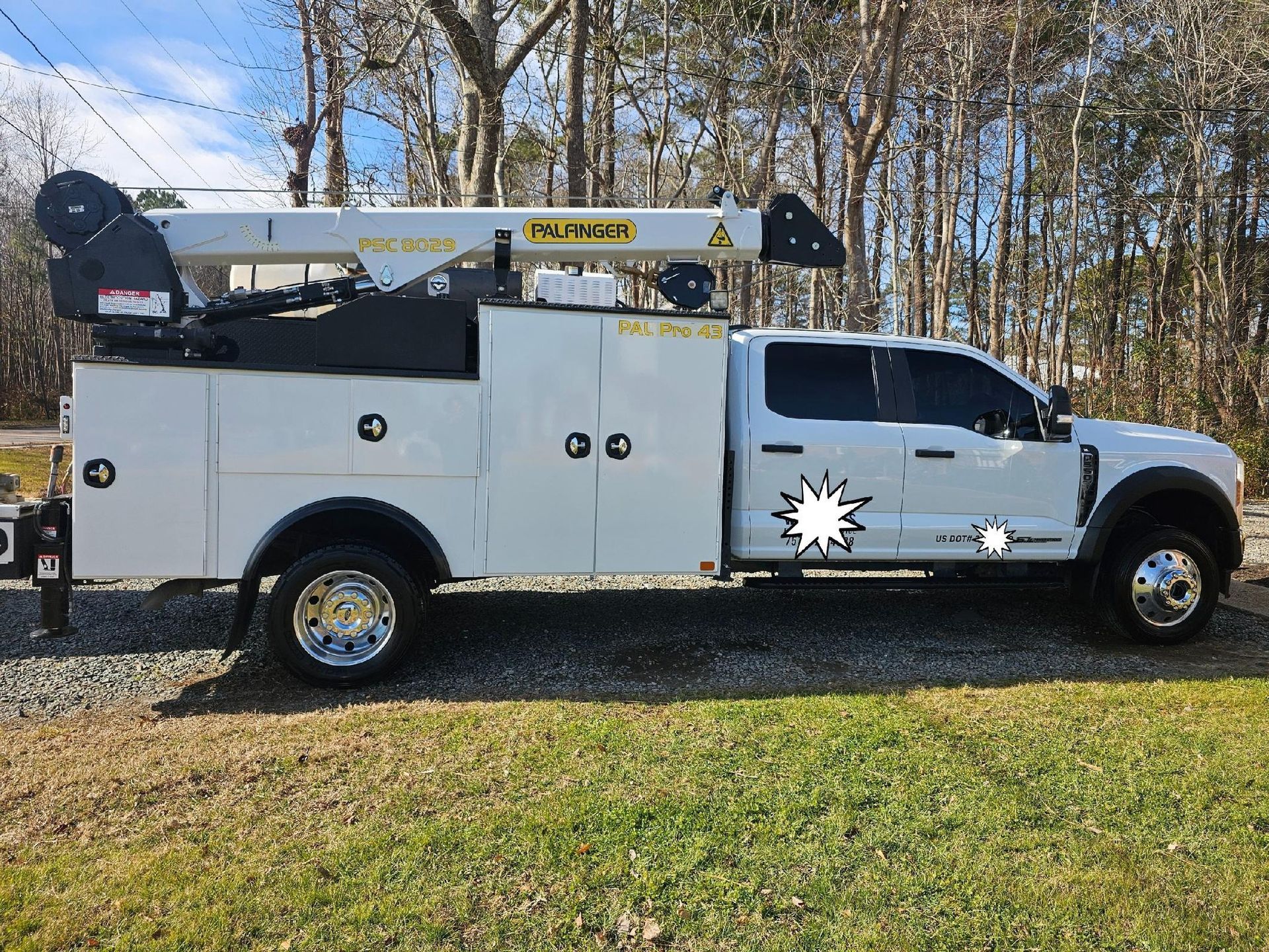 White utility truck with an articulated boom lift parked on grass.