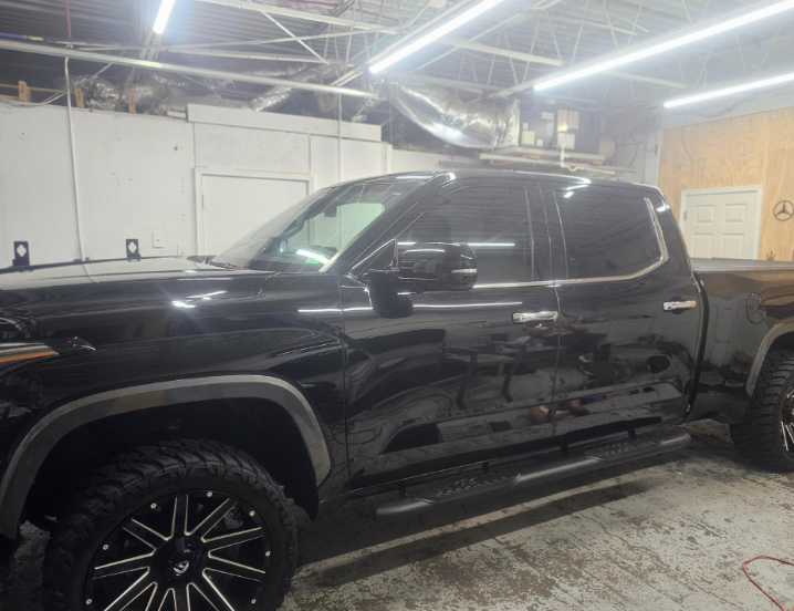 Black pickup truck in a garage; tinted windows, black rims, running boards.