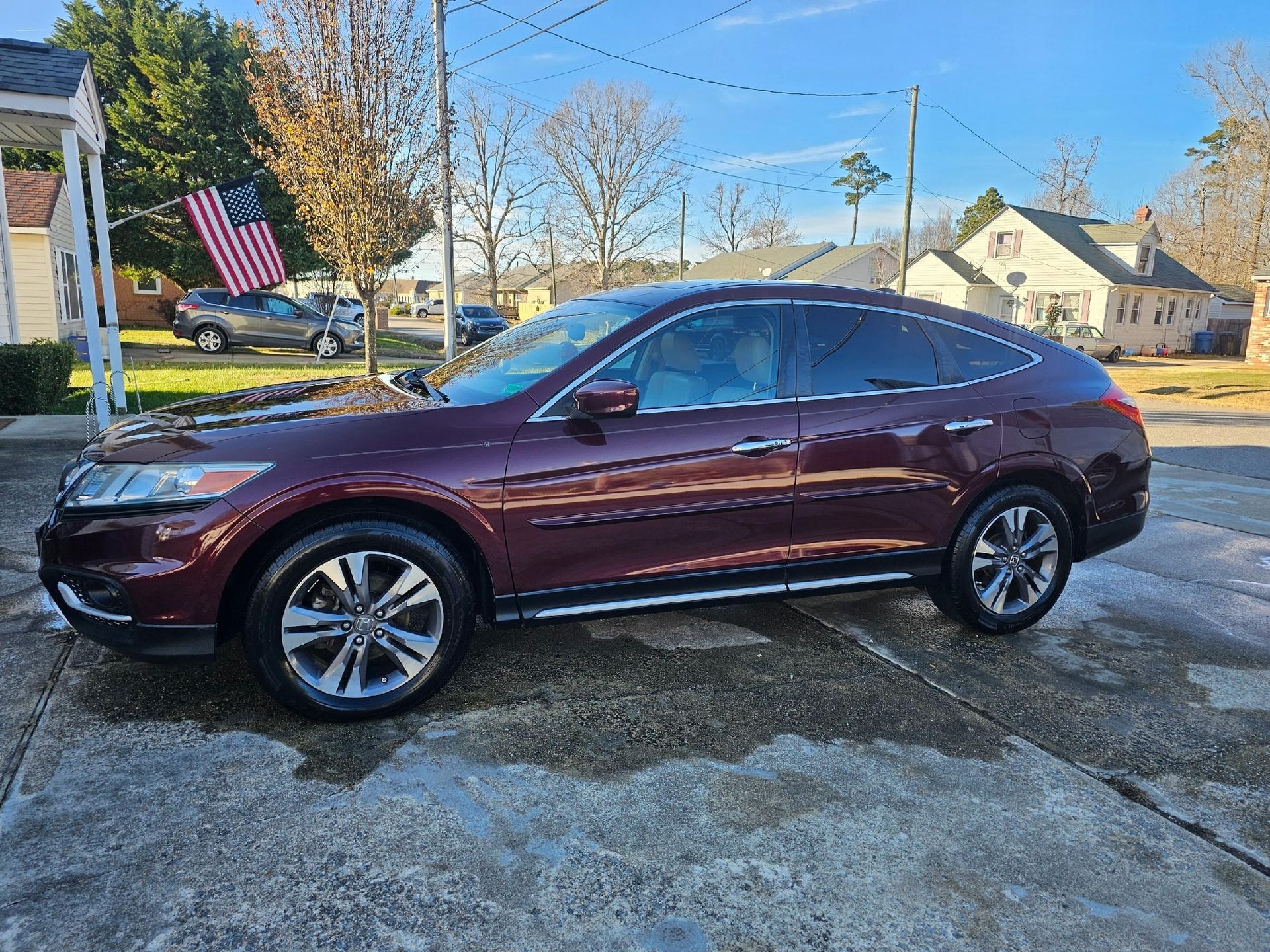 Maroon Honda Crosstour parked on a wet surface outdoors; American flag in the background.