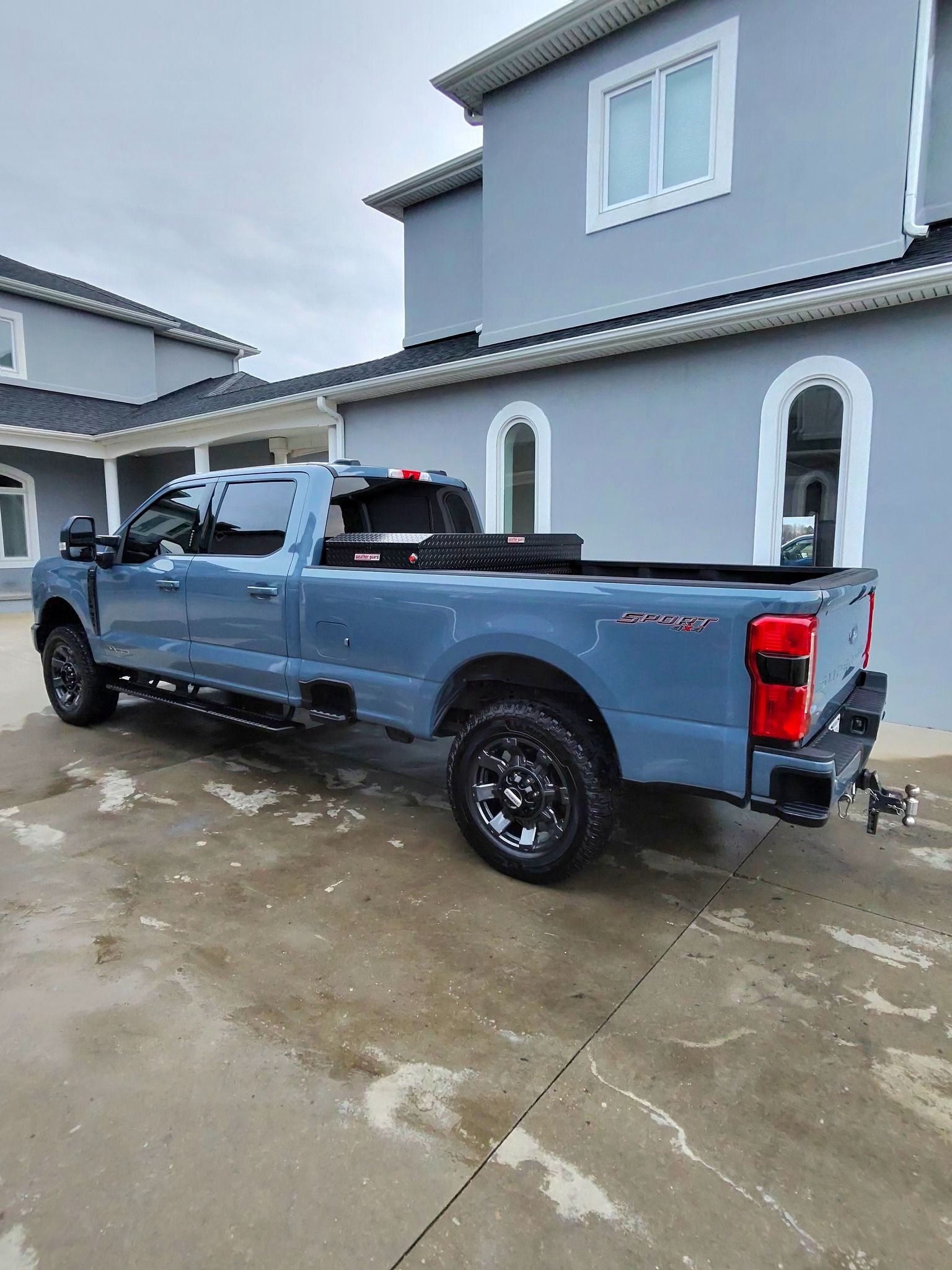 Blue pickup truck parked in front of a light blue building on a cloudy day.