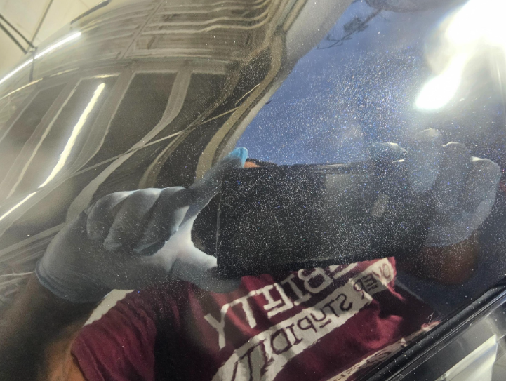 Person using a black device to clean a reflective surface with a maroon shirt and gray gloves visible.