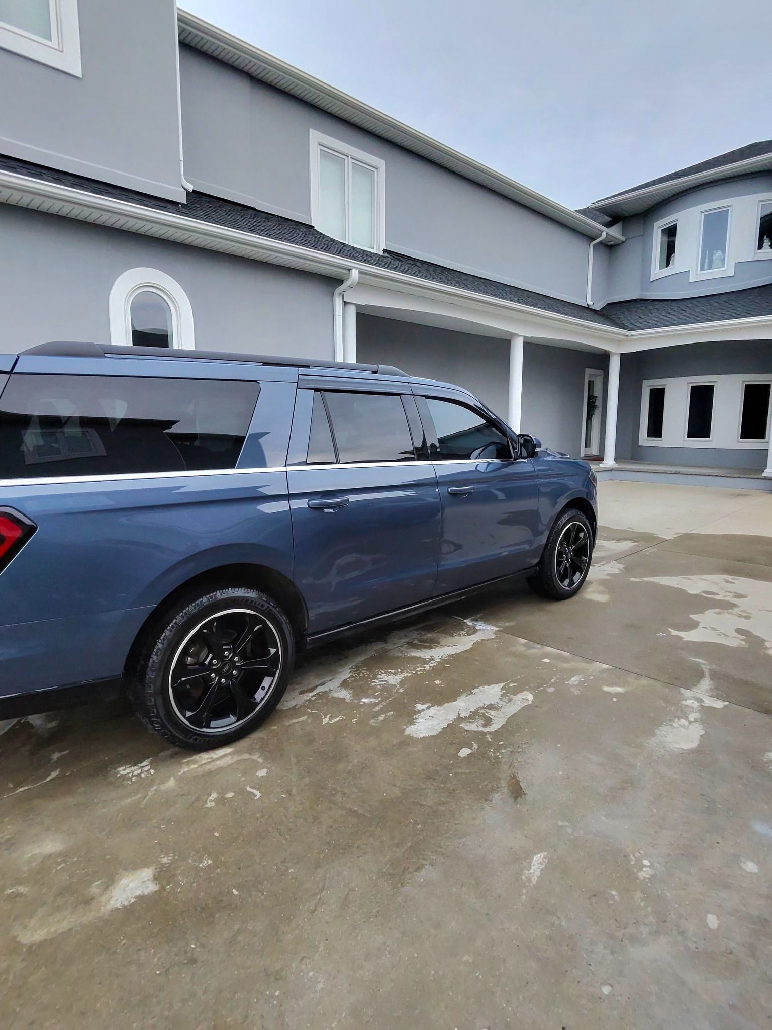 Blue SUV parked in front of a light gray house with black trim and windows.