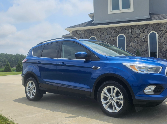Blue Ford Escape SUV parked on a driveway in front of a house.
