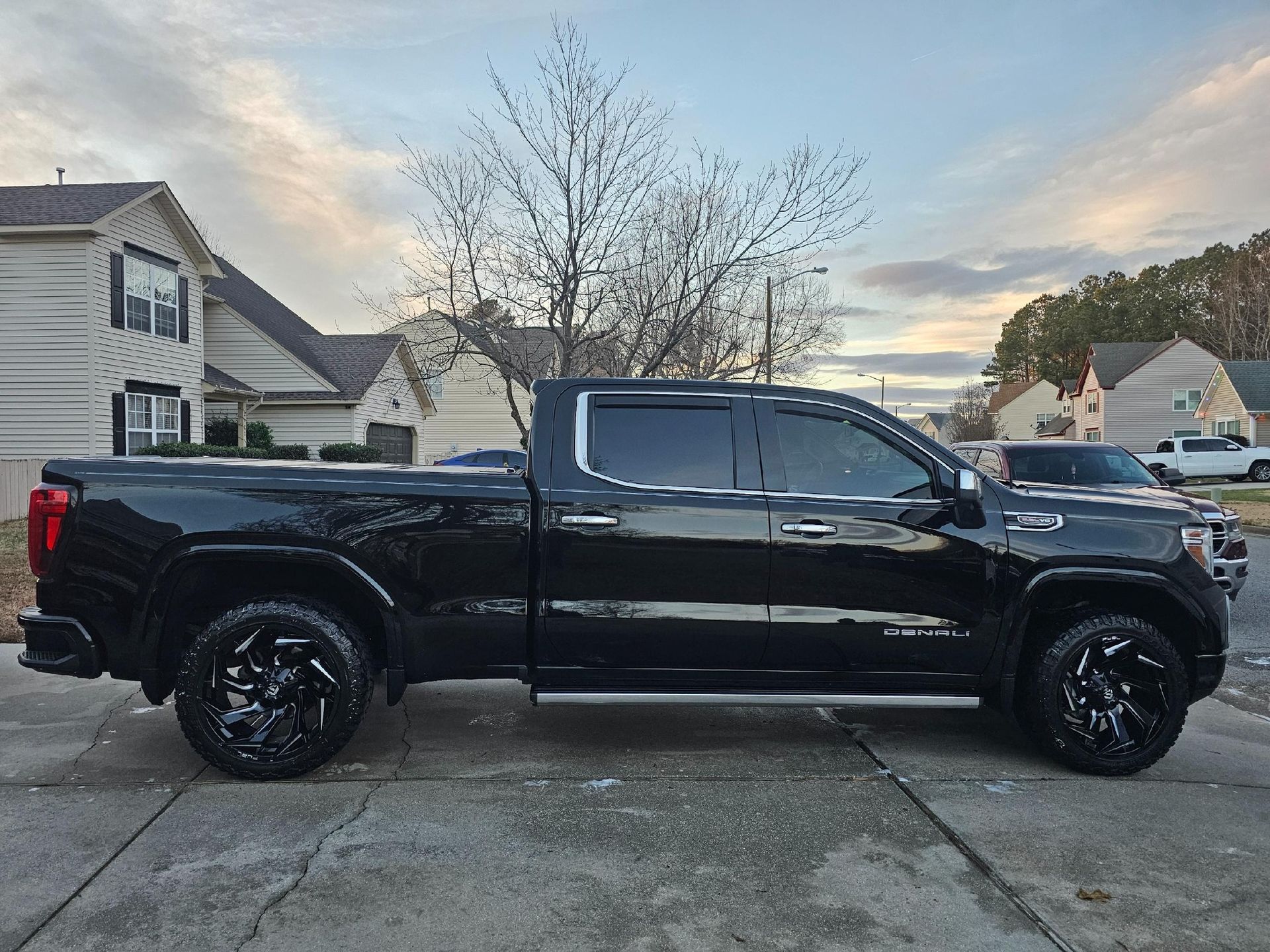 Black pickup truck parked on a driveway with tinted windows, black wheels, and a cloudy sky background.