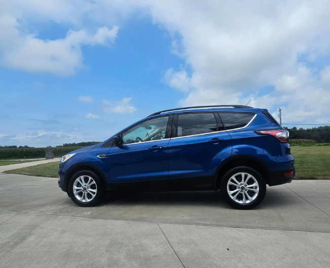 Blue Ford SUV parked on concrete against a blue sky with clouds.