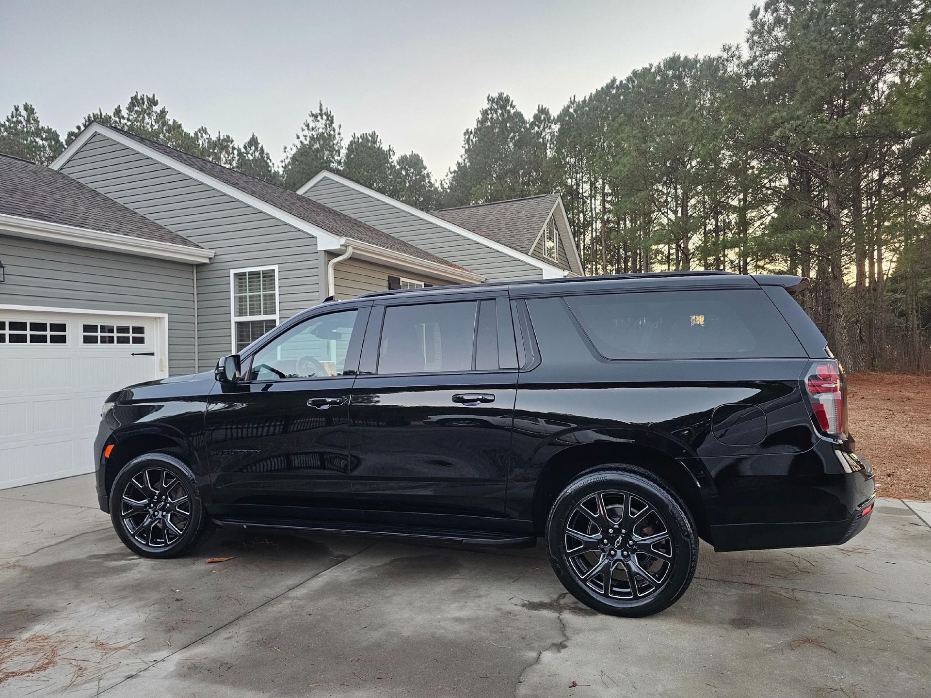 Black SUV parked in front of a gray house with a white garage door, trees in the background.