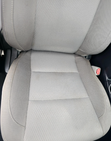 Beige car seat. Seat has three padded sections.  A red seatbelt buckle is visible.