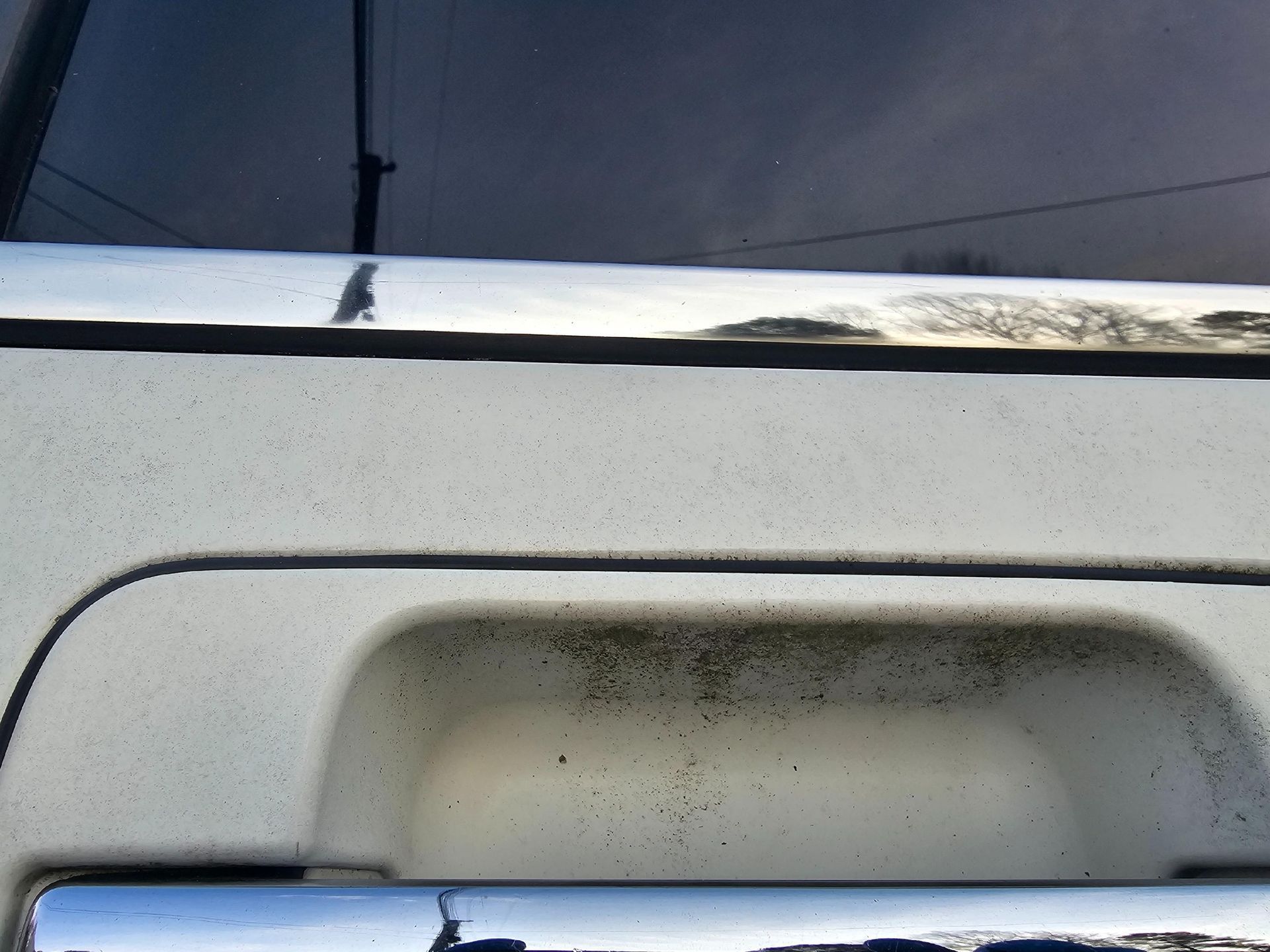 White truck tailgate with chrome accents, showing dirt and weathering.