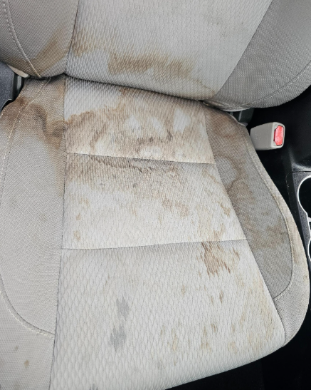 Beige car seat stained with brown dirt and spots.