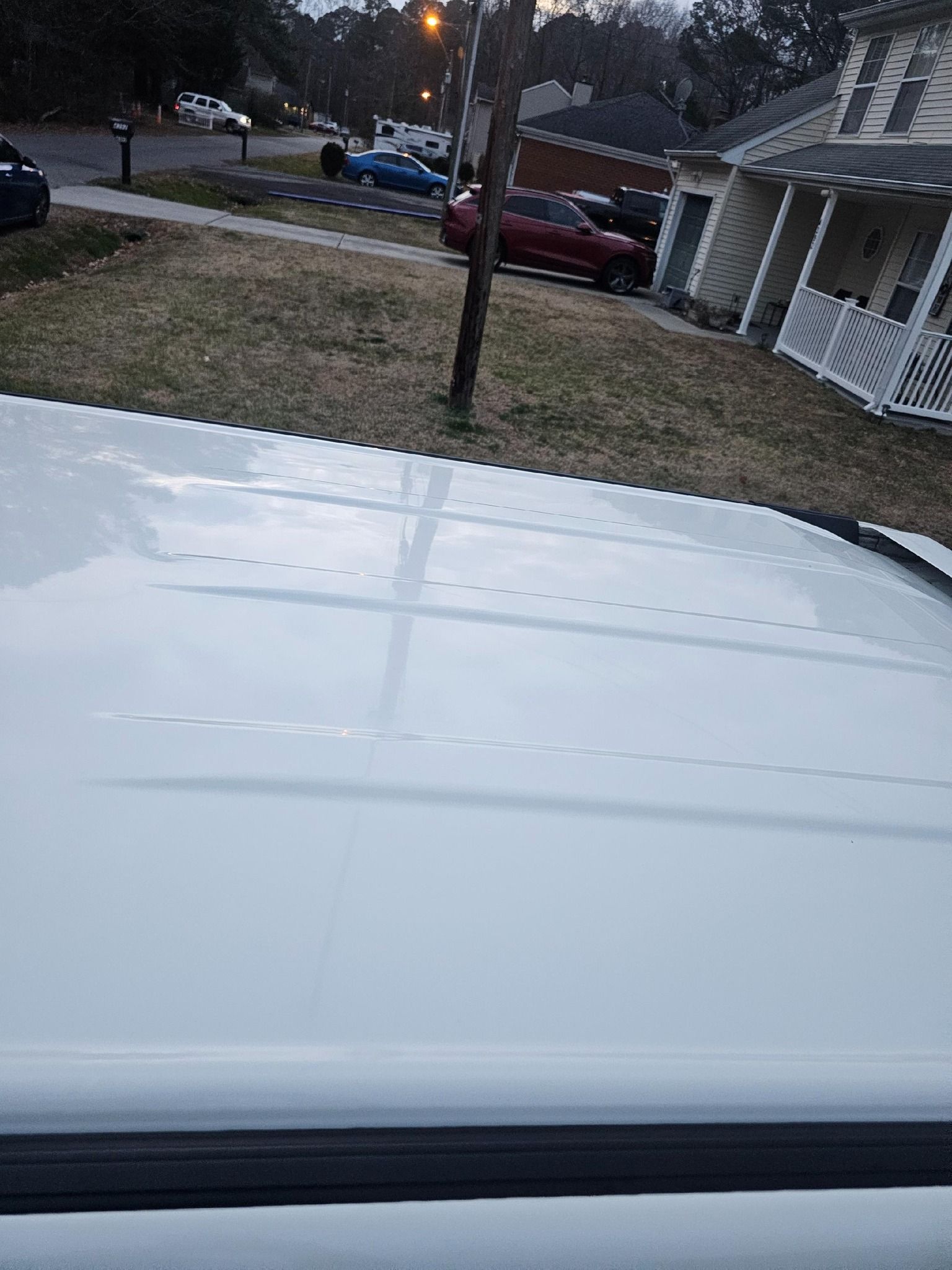 White car roof with reflections, residential street in background with parked cars.