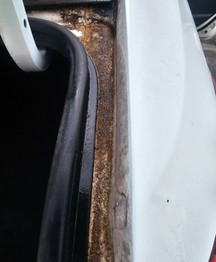 Rust and grime buildup on the edge of a white car trunk opening near the seal.