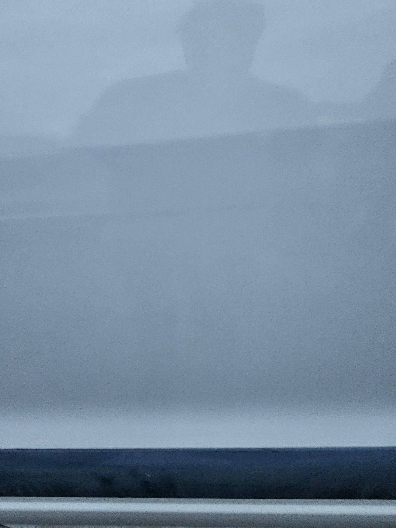 Reflection of a person in a slightly blurred, white surface. A dark blue line is visible at the bottom.