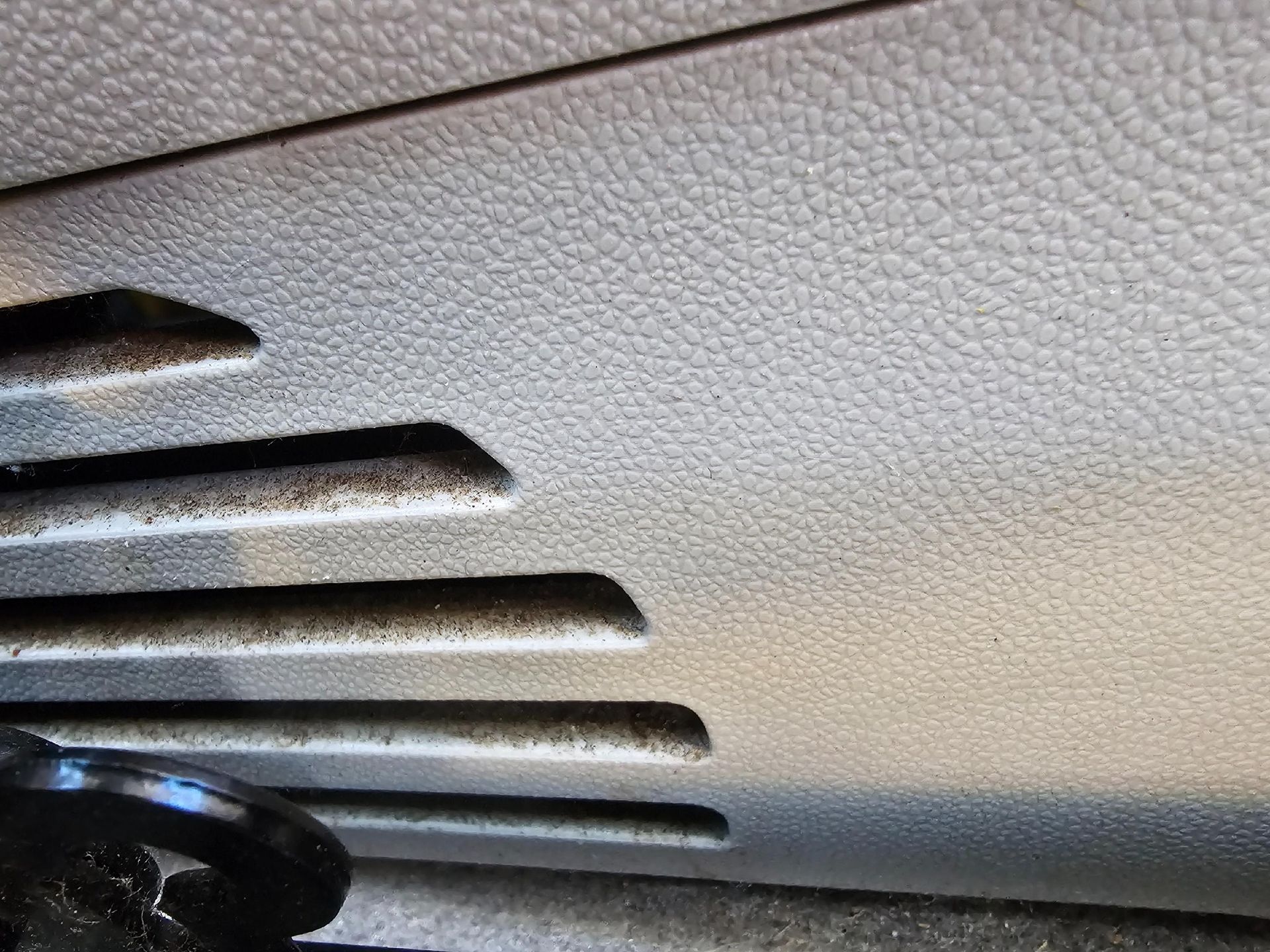 Close-up of a car's gray dashboard with air vent slits and textured surface.