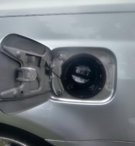 Open car gas tank door; black gas cap attached with a black tether.