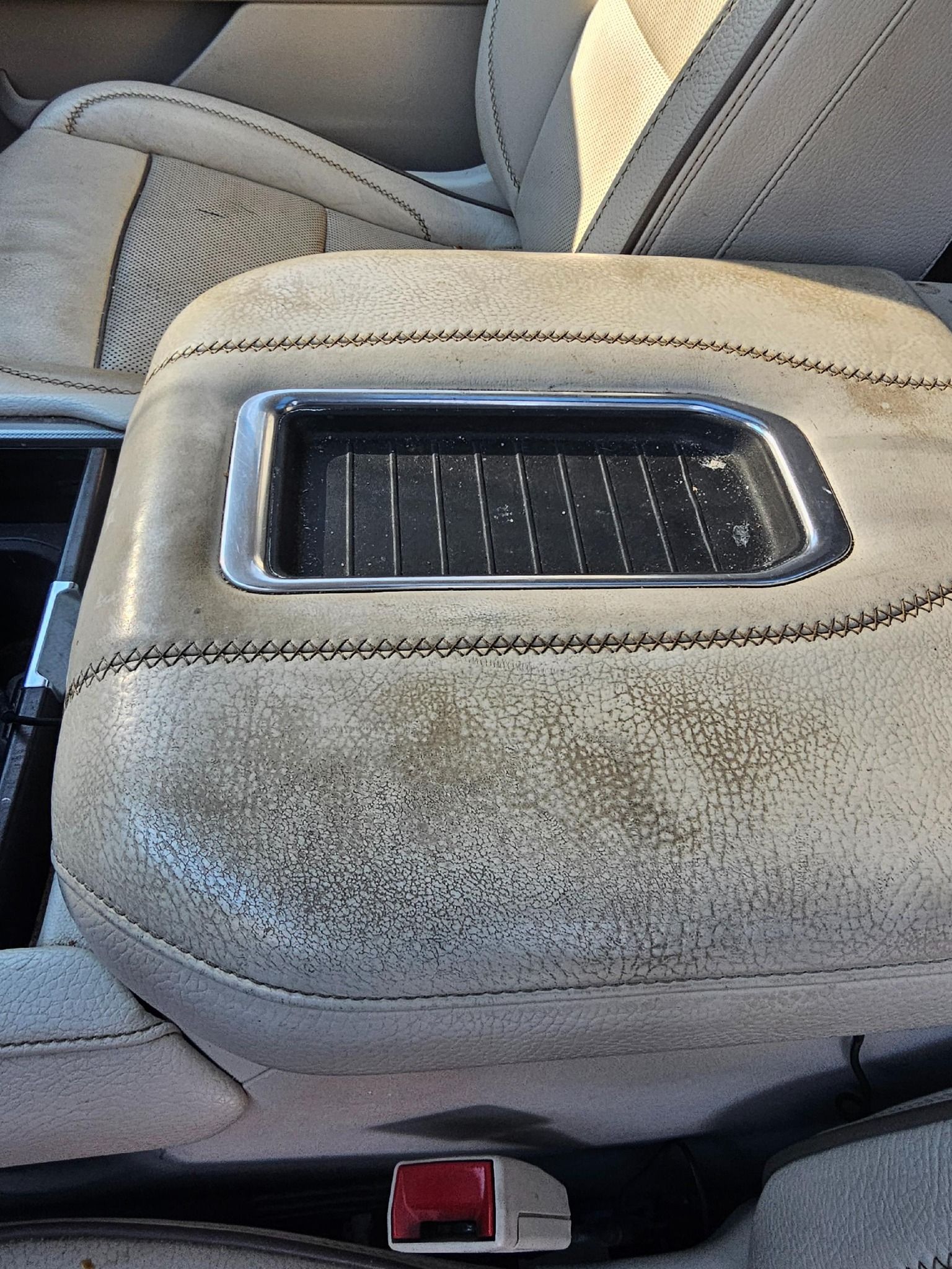 Car's center console with worn, light-colored upholstery, a chrome-trimmed tray, and a visible seatbelt buckle.
