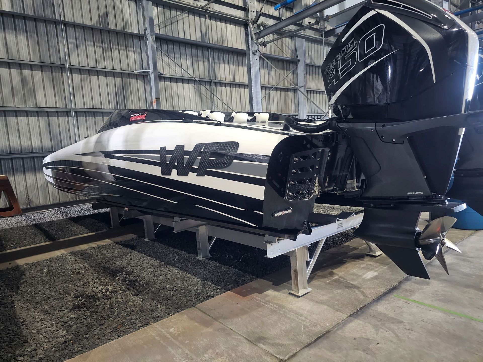A sleek, black and white powerboat with large outboard motor on a stand in a garage.