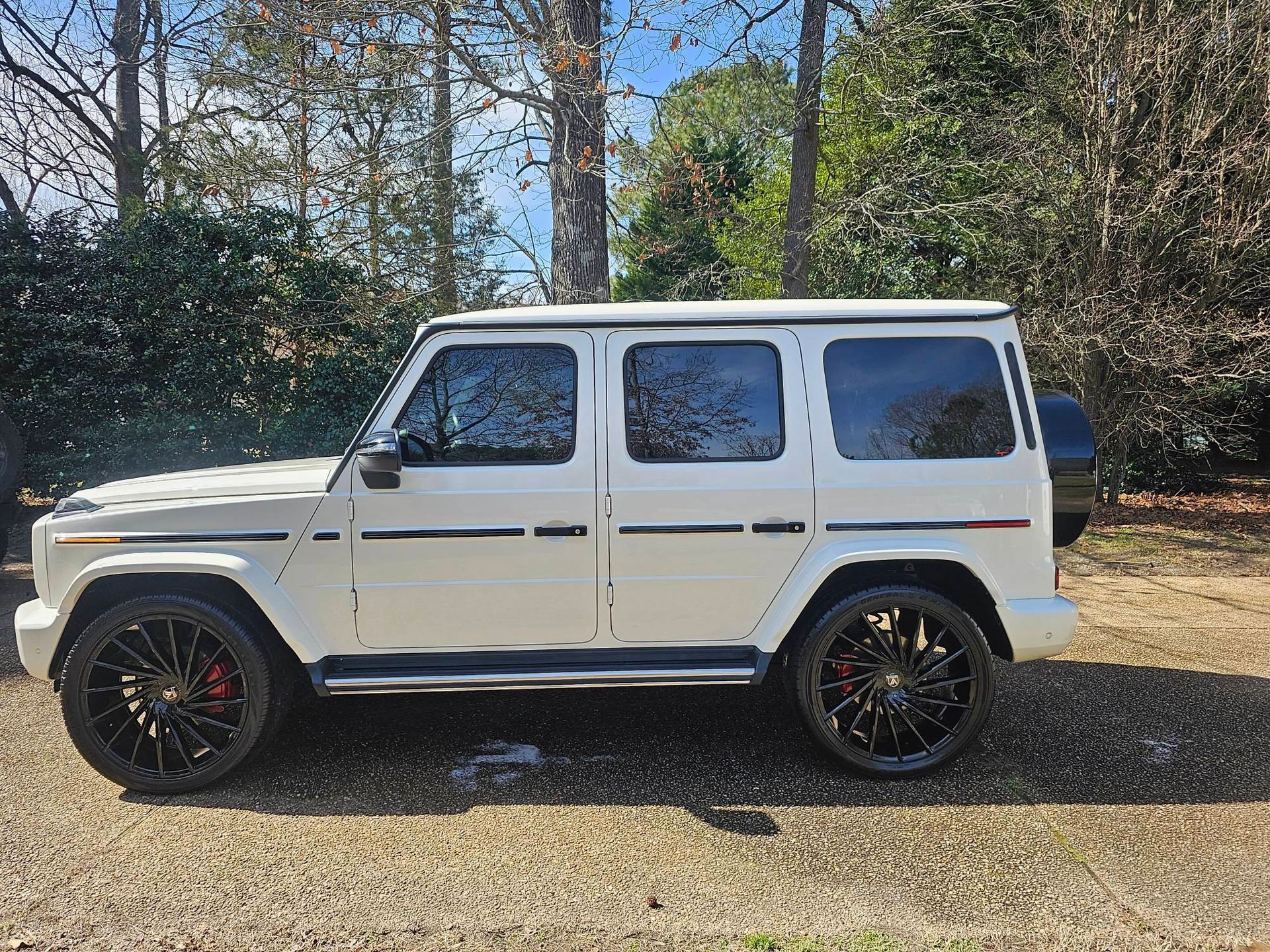 White Mercedes-Benz G-Wagon SUV with black rims parked outside on a sunny day.