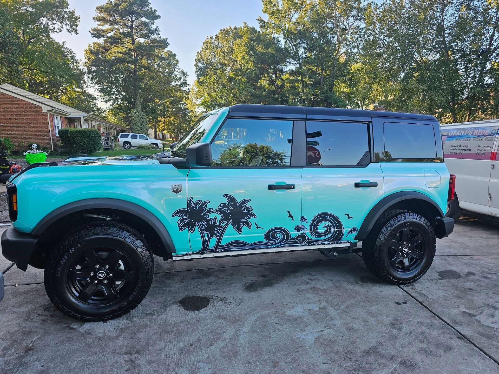 Teal Ford Bronco with black accents, palm tree decals, parked outside on concrete.