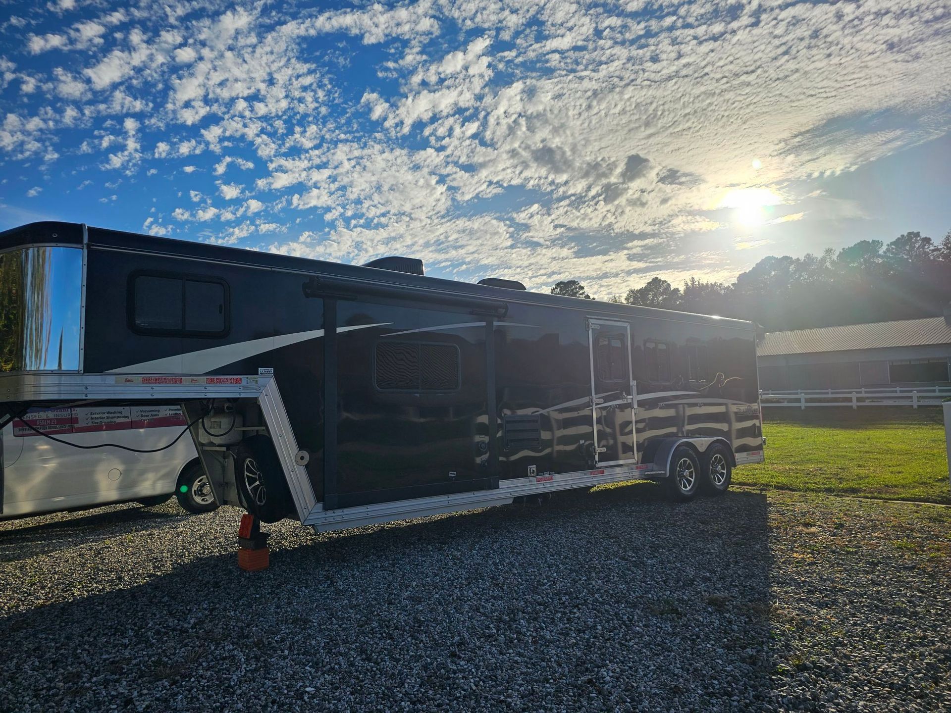 Black horse trailer parked on gravel with sunny sky backdrop.