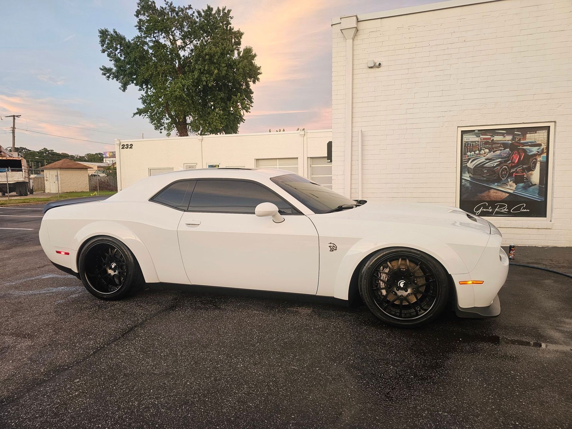 White Dodge Challenger parked by a building with a mural; overcast sky.