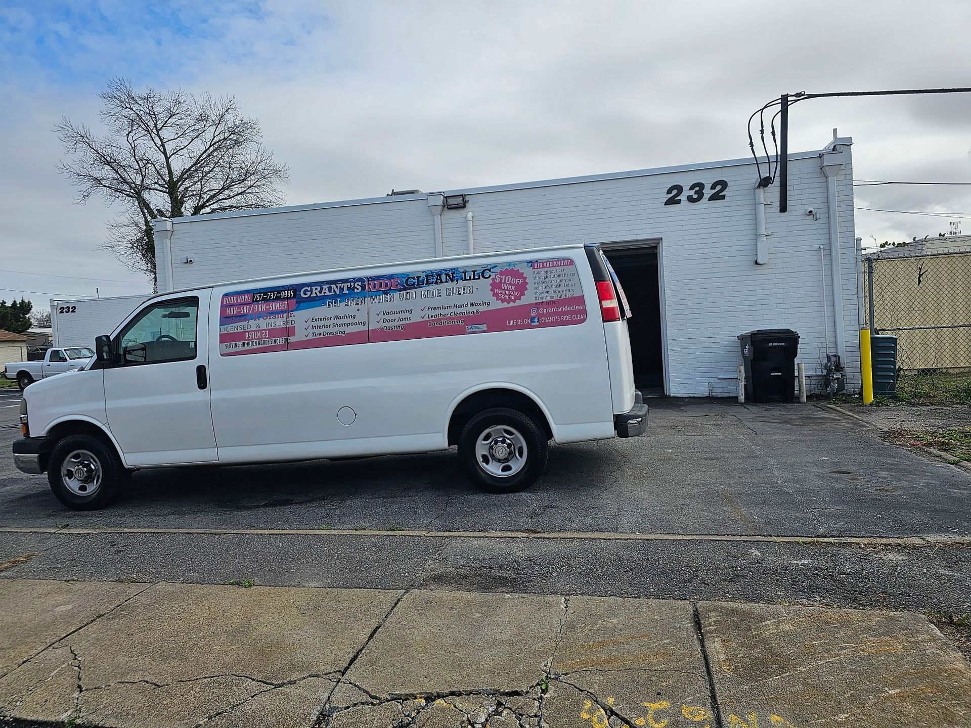 White van with company logo parked outside a white building with the number 232.