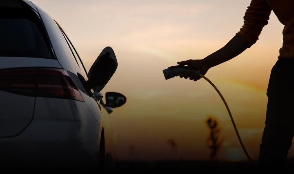 A person is charging an electric car at sunset