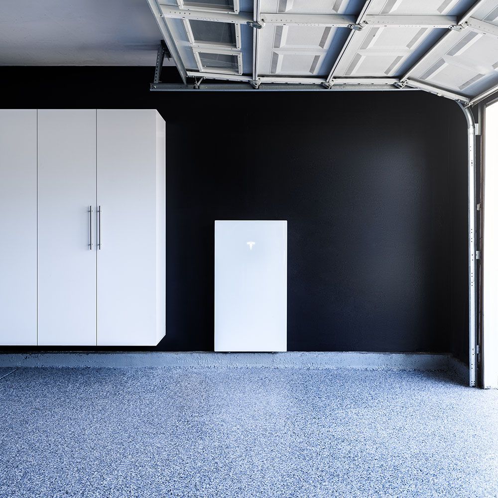 Garage interior with white cabinets and a battery, door open. Blue speckled floor, black wall.