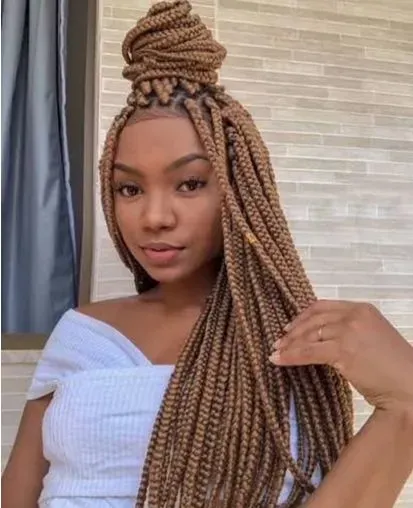 Woman with long, light brown box braids, half-up in a bun, wearing an off-the-shoulder white top.