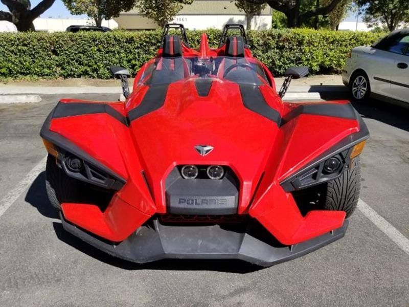 Red Polaris Slingshot three-wheeled vehicle parked in a parking lot.