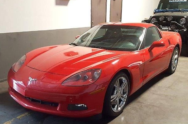 Red Corvette sports car parked in a garage with a black Jeep visible in the background.