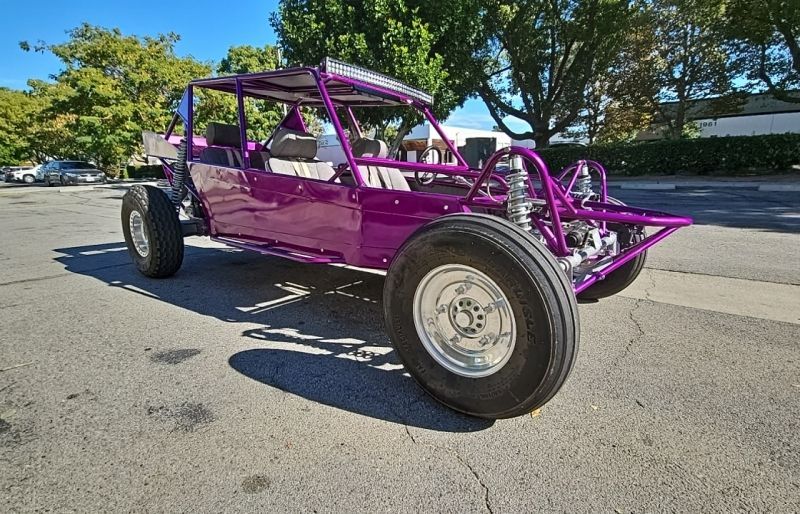 Purple dune buggy parked on a paved surface. It has roll bars, large tires, and a roof-mounted light bar.