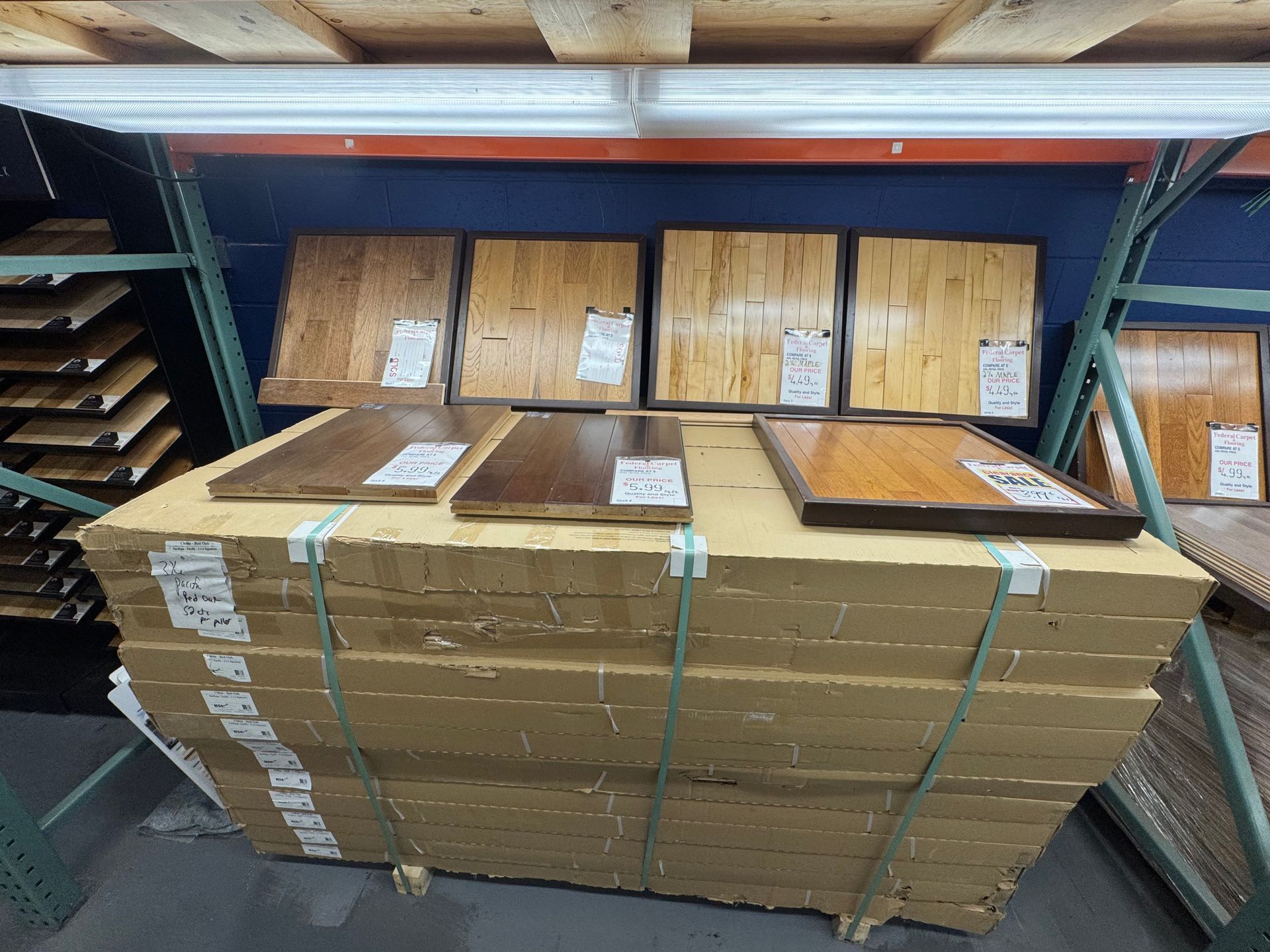 Pallet of hardwood flooring samples in a warehouse, featuring various wood tones and textures.