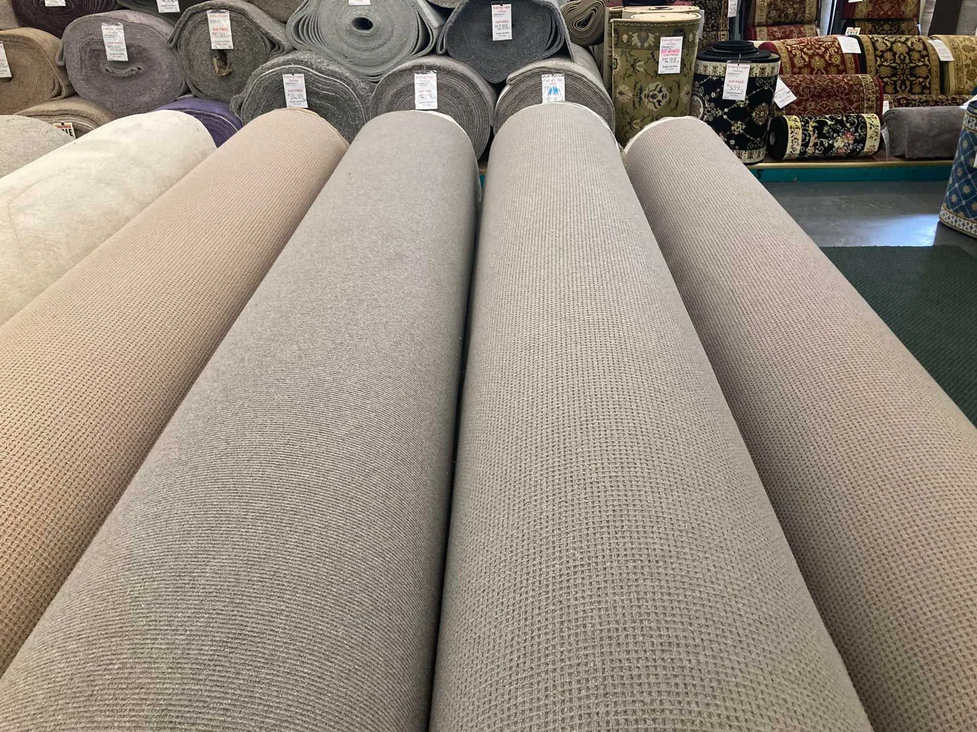 Rows of rolled-up carpets in various neutral colors.  Warehouse setting.