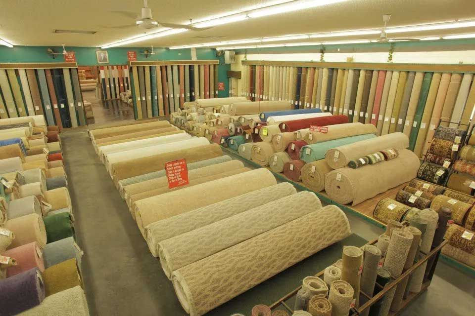Carpet store interior with rows of rolled carpets, various colors.