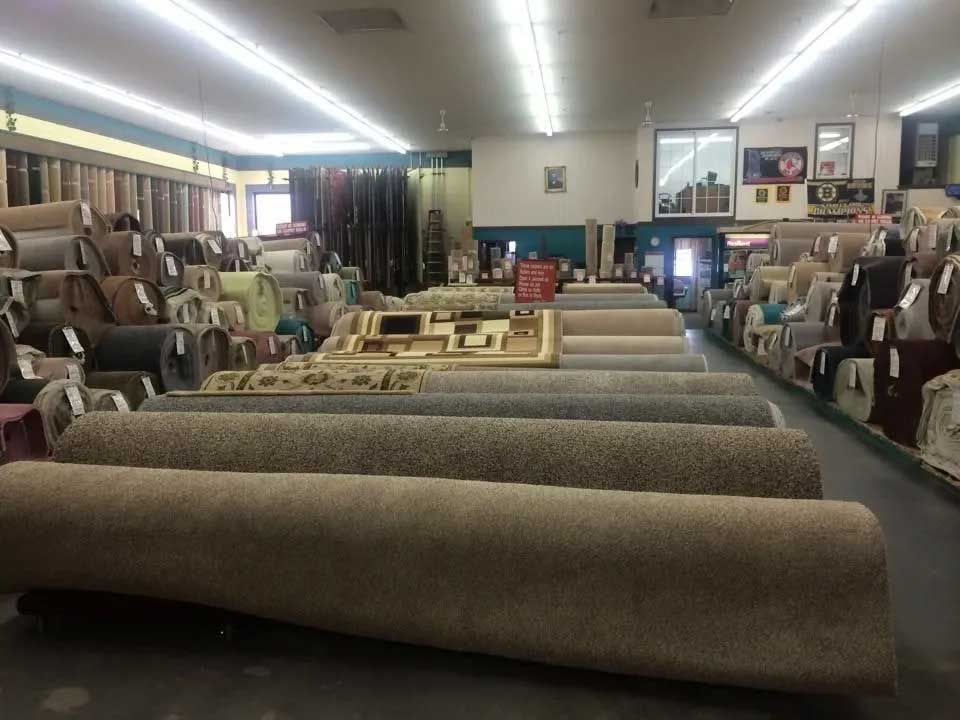 Rows of rolled carpets in a store, various colors and textures, bright lighting, a carpet showroom.