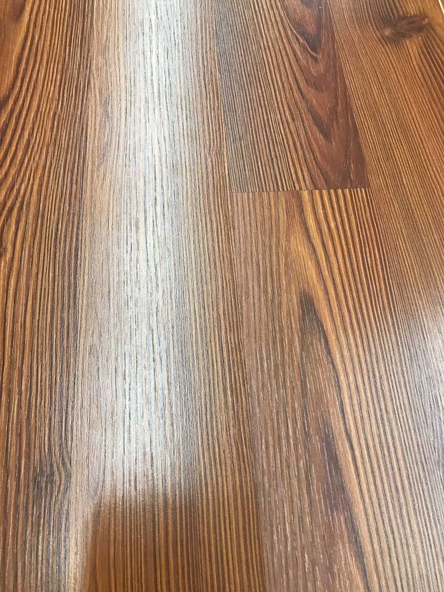 Brown wood-look laminate flooring with a significant white residue in the center.