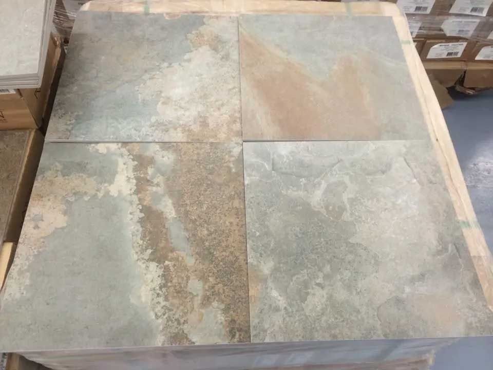 Four irregularly shaped slate tiles on a pallet, varying shades of green, tan, and rust.