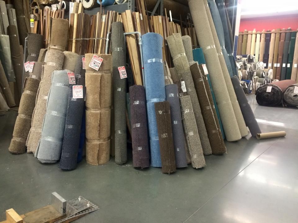 Rolled carpet samples of various colors and textures are stacked in a retail setting.