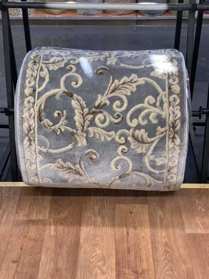 Rug with floral design, wrapped in plastic, on a wooden floor.